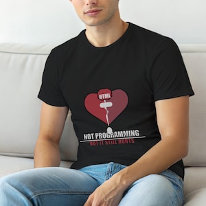 Op de afbeelding: Zwart t-shirt met een grafisch ontwerp met een rood hart met een gebroken lijn en het woord "HTML" erboven. Onder het hart staat de tekst "NOT PROGRAMMING BUT IT STILL HURTS."