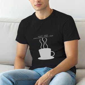 Könnte beinhalten: Schwarzes T-Shirt mit einer weißen Grafik einer dampfenden Kaffeetasse und dem Text "SELECT FROM COFFEE WHERE AWAKE = TRUE". Das Design ist mittig auf der Brust platziert.