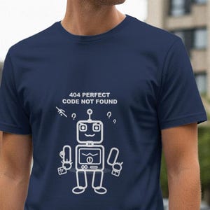 Könnte beinhalten: Marineblaues T-Shirt mit weißer Roboter-Grafik und dem Text "404 PERFECT CODE NOT FOUND". Das Roboter-Design umfasst einen Kopf mit Antenne, einen Bildschirm und Arme, die Werkzeuge halten. Das Shirt ist aus weichem Material.