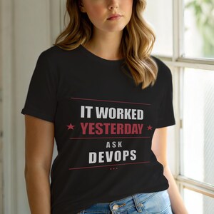 Op de afbeelding: Zwart T-shirt met de witte en rode tekst "IT WORKED YESTERDAY ASK DEVOPS". Het shirt heeft een ronde hals en korte mouwen. De tekst staat in het midden op de voorkant.