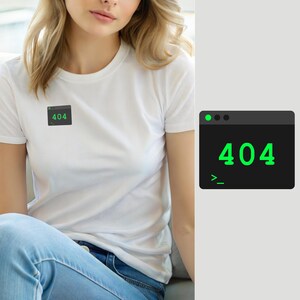 Puede incluir: Una camiseta blanca de manga corta con un pequeño gráfico rectangular en el pecho. El gráfico es una ventana de terminal de computadora gris oscuro con un punto verde, el texto 404 en fuente verde grande y un símbolo de línea de comandos.