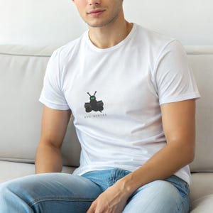 May include: White t-shirt featuring a black bug graphic and the words "BUG HUNTER". The design shows a stylized bug with green eyes and antennae. The shirt is made of a soft, comfortable material.