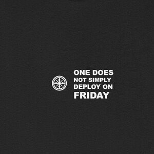 May include: Black t-shirt with white text and a circular graphic. The text reads "ONE DOES NOT SIMPLY DEPLOY ON FRIDAY". The shirt is made of a soft material and has short sleeves.
