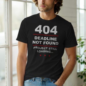 May include: Black crew neck t-shirt with the text "404 DEADLINE NOT FOUND PROJECT STILL LOADING..." in white and red. The shirt is a casual wear item.