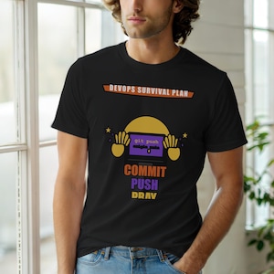 May include: Black t-shirt with a graphic design. The design includes the text "DEVOPS SURVIVAL PLAN" above a cartoon laptop with the words "git push" on the screen. Below the laptop, the words "COMMIT PUSH DRAV" are printed in orange and purple.