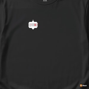 Può includere: T-shirt nero con un motivo a robot pixelato. Il robot è bianco con dettagli rossi e bianchi. La maglietta è realizzata in cotone pesante.
