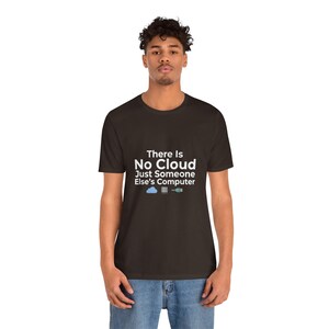 Peut inclure: T-shirt marron foncé avec le texte "There Is No Cloud Just Someone Else's Computer" en blanc. Le t-shirt présente un nuage et un graphique d'ordinateur. La personne porte un jean bleu.