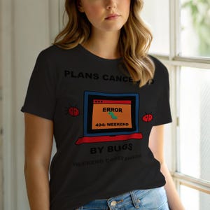May include: Black t-shirt with a humorous computer-themed graphic. The design features a laptop with an error message that reads "ERROR 404: WEEKEND" and the text "PLANS CANCELLED BY BUGS". Two ladybug graphics are on the shirt.
