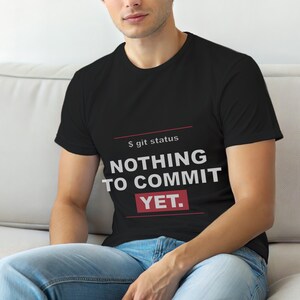 May include: Black t-shirt featuring the text "S git status NOTHING TO COMMIT YET." in white and red. The shirt has a crew neck and is being worn.