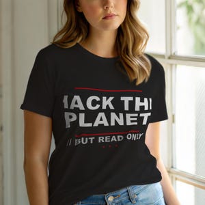 Op de afbeelding: Zwart T-shirt met de witte tekst "HACK THE PLANET", met een rode lijn erboven en eronder. Daaronder staat "BUT READ ONLY" in het wit.