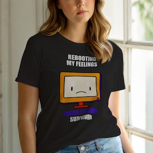 Może przedstawiać: Czarny t-shirt z kreskówkowym komputerem z smutną twarzą. Tekst "REBOOTING MY FEELINGS" znajduje się powyżej, a "PATCH TUESDAY SURVIVOR" poniżej. Komputer ma żółtą ramkę. Casualowy t-shirt z grafiką.