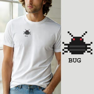 May include: A white short-sleeved t-shirt featuring a small pixel art graphic on the chest. The graphic depicts a black insect with red eyes and the word BUG printed in a simple black font directly underneath the pixelated creature design.