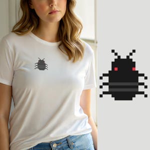 Puede incluir: Una camiseta blanca de manga corta con un pequeño gráfico de pixel art de un escarabajo negro con dos ojos rojos y dos rayas horizontales grises en la espalda, situado en la zona del pecho izquierdo de la prenda.