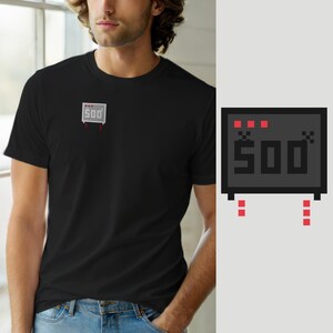 Puede incluir: Una camiseta negra de manga corta con un pequeño gráfico centrado en el pecho que muestra una pantalla de televisión gris pixelada con el texto 500, tres cuadrados rojos encima y dos filas verticales de tres cuadrados rojos debajo.