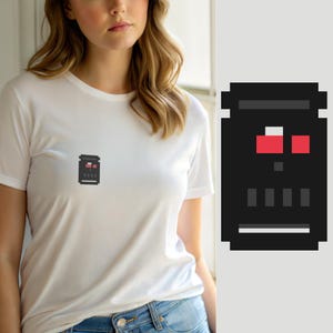Peut inclure: Un t-shirt blanc à manches courtes avec un petit motif en pixel art centré sur la poitrine. Le motif est une forme rectangulaire noire avec deux carrés rouges, un petit carré blanc, un point gris, quatre barres grises et une ligne grise.