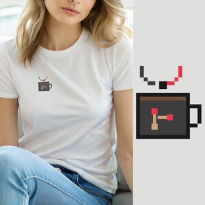 May include: A white short-sleeved t-shirt featuring a small pixel art graphic on the chest. The graphic depicts a dark gray coffee mug with a brown liquid interior and a red and tan hammer icon, with a pixelated steam trail above the mug.