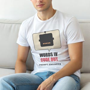 Könnte beinhalten: Weißes T-Shirt mit einem Roboter-Grafik in einer Sprechblase. Der Text lautet "WORDS IN CODE OUT" in Schwarz und Rot, darunter "PROMPT ENGINEER". Das T-Shirt wird von einer Person getragen.