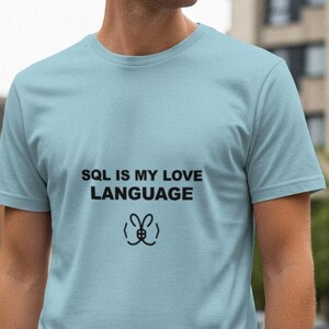 May include: A pale blue t-shirt featuring the black text "SQL IS MY LOVE LANGUAGE" and a small graphic. The short-sleeved shirt is made of a soft fabric.
