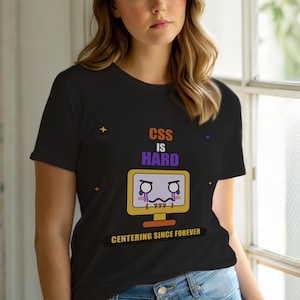 Op de afbeelding: Zwart T-shirt met de tekst "CSS IS HARD" boven een huilende computermonitorafbeelding. De zin "CENTERING SINCE FOREVER" staat eronder. Het shirt heeft een ronde hals en korte mouwen.