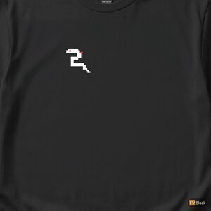May include: Black t-shirt featuring a pixelated white snake design with red accents. The snake is positioned on the upper left chest area. The shirt is made of heavy cotton.