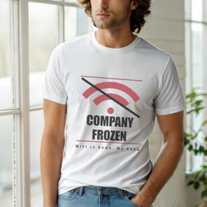 Op de afbeelding: Wit T-shirt met ronde hals met een rood en zwart grafisch ontwerp van een doorgestreept wifi-symbool. De tekst op het shirt luidt "COMPANY FROZEN" en "WiFi is Down. We Know."