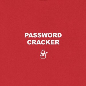 May include: A red t-shirt with the words "PASSWORD CRACKER" in white block letters. Below the text is a small white graphic of a lock and a key. The shirt is made of a soft material.