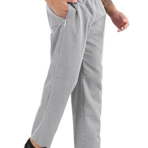 May include: Full-length trousers featuring a small black and white checkered pattern. These pants have an elasticized waistband, side pockets, and a straight-leg cut. The fabric displays a consistent micro-check design throughout the garment.