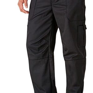 May include: Black work pants with multiple pockets and a relaxed fit. The pants have an elastic waistband and are worn with black shoes. The image shows the pants from the waist down, with a person's hand in the pocket.