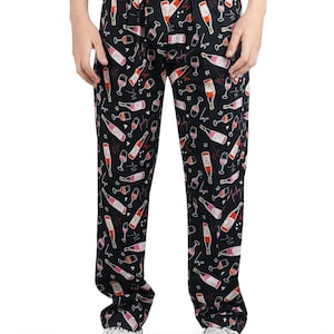 May include: Black lounge pants featuring an all-over print of wine bottles, wine glasses, and the word love in cursive script. The pants have an elastic waistband and a relaxed fit, showcasing a repeating pattern in shades of pink, red, and white.
