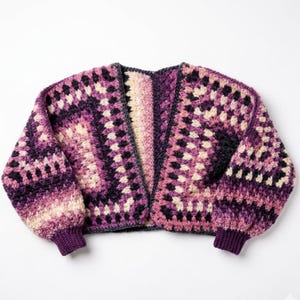 Puede incluir: Un cárdigan de crochet hecho a mano, sin cierre, en tonos morado, rosa y crema. El patrón de cuadrados de la abuela presenta un degradado de color, con tonos más oscuros en los puños y las mangas. Las mangas son largas y los puños están acanalados.