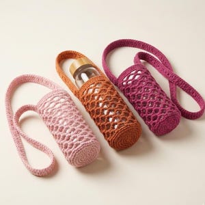 Puede incluir: Tres portabotellas de agua de ganchillo hechos a mano en tonos rosa, naranja y morado. Cada soporte tiene una correa y un diseño similar a una red. Un soporte contiene una botella de agua de vidrio con tapa de madera.