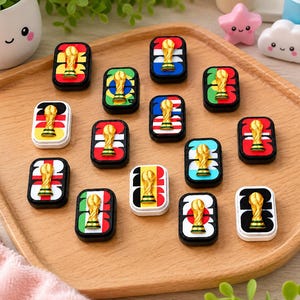 May include: A collection of rectangular pins featuring the number 2026 with a gold-colored trophy icon centered on various national flag backgrounds. Each pin has a black or white border and displays distinct flag colors including red, yellow, green, blue, and white.