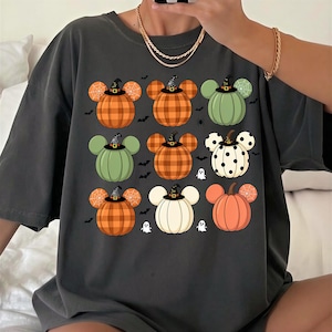 May include: A charcoal gray short-sleeve t-shirt featuring a graphic print of nine pumpkin shapes with mouse-like ears, each wearing a small black witch hat. The pumpkins display various patterns including plaid, polka dots, and spider webs.