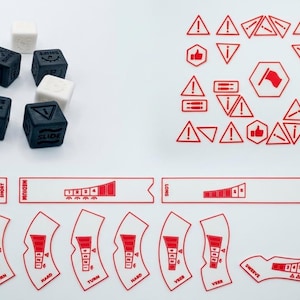 Peut inclure: Un ensemble de dés cubiques noirs et blancs avec des icônes et du texte gravés, accompagné d'une feuille d'autocollants rouges présentant divers symboles d'avertissement, des flèches directionnelles et des étiquettes incluant le mot SLIDE.