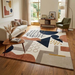 May include: A rectangular rug with a cream base and a geometric pattern in navy, rust, grey, and gold. The rug is placed in a living room, featuring a sofa, coffee table, and artwork. The rug's design incorporates various shapes and lines.