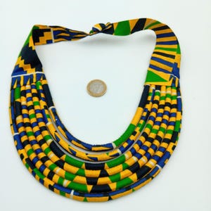 Peut inclure: Un collier multi-rangs vibrant avec un imprimé africain coloré. Le collier présente un motif répétitif de formes géométriques jaunes, bleues, vertes et noires. Le collier est noué en haut et il y a une pièce de monnaie à côté.