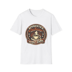 Può includere: T-shirt bianca con grafica circolare. La grafica recita "Apprentice Electrician" e "Powered by Coffee", con una tazza di caffè e un design a vapore. Il design utilizza colori marrone, arancione e nero.