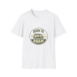 Puede incluir: Camiseta blanca con un gráfico circular que presenta una furgoneta camper, árboles y el texto "BORN TO ROAM" en verde y beige. La camiseta tiene mangas cortas y cuello redondo.