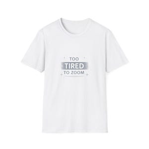 Può includere: T-shirt bianca con girocollo e maniche corte. La maglietta presenta la scritta "TOO TIRED TO ZOOM" in un design rettangolare argentato. Piccole forme a stella sono sopra e sotto il testo.