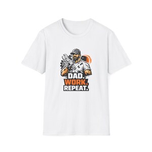 Può includere: T-shirt bianca con grafica di un uomo che tiene una chiave inglese, con la scritta "DAD. WORK. REPEAT." in arancione e nero. L'uomo indossa un berretto e ha la barba. Il disegno è centrato sulla maglietta.