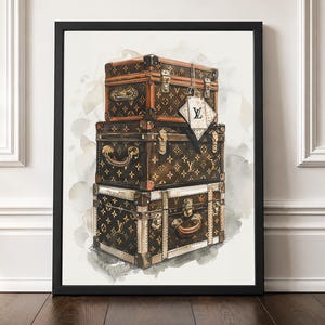 May include: A framed print showing a watercolour illustration of three stacked vintage travel trunks. The trunks are brown with gold hardware and a repeating logo pattern. A tag with a logo hangs from the top trunk.