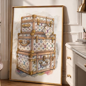 May include: A framed wall art print featuring a watercolor illustration of three stacked vintage-style trunks. The trunks are white with a multicolored monogram pattern, gold-toned metal hardware, and leather-look trim, presented in a gold frame.