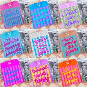 May include: Nine brightly coloured t-shirts with different slogans and designs. Each shirt has a different colour, like pink, blue, and orange, with vertical striped patterns and text such as "Sweet Summer Time" and "Mama Needs a Margarita."