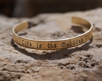 May include: Gold-toned metal bracelet with the inscription "Life is the Bubbles" and a small heart symbol.