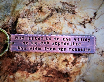 May include: A copper-colored keychain with the inscription "God takes us to the valley so we can appreciate the view from the mountain."