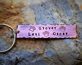 May include: A copper-colored metal keychain with three paw prints and the names "Grover", "Levi", and "Oscar" engraved on it.