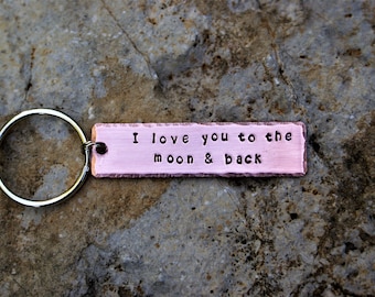 May include: A silver key chain with a pink metal tag that reads "I love you to the moon & back".
