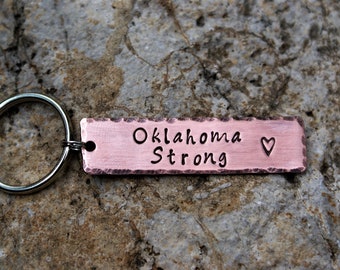 May include: A copper keychain with a rectangular tag that reads "Oklahoma Strong" with a small heart symbol.
