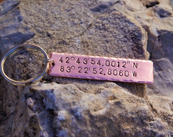 May include: A copper keychain with a silver ring and engraved coordinates: 42° 43' 54.0012" N 83° 22' 52.8060 W.