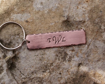 May include: A copper keychain with a silver key ring. The copper tag is rectangular and has a hammered texture. The initials "T.W.L." are engraved on the tag.